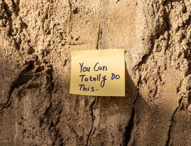 A sticky note with a motivational message on a textured wall in Dubai, with sunlight casting shadows.